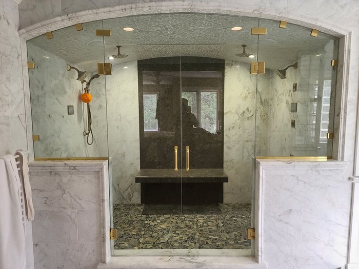 Frameless double-door shower enclosure with satin brass hardware and an arched marble surround