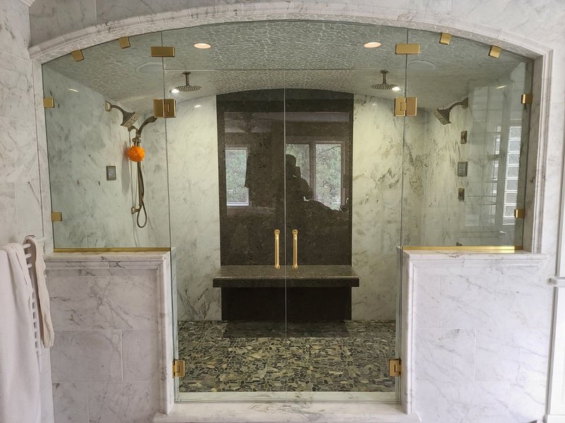 Frameless double-door shower enclosure with satin brass hardware and arched marble surround