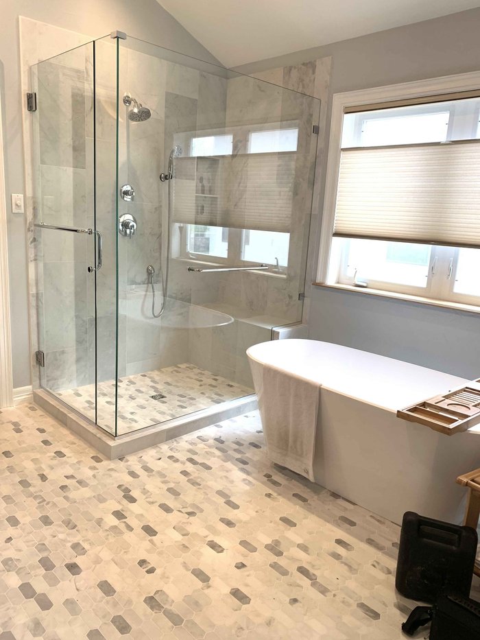 Frameless shower enclosure with chrome clips beside a marble soaking tub