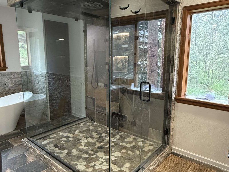 Frameless steam shower enclosure with stone surround and black hardware