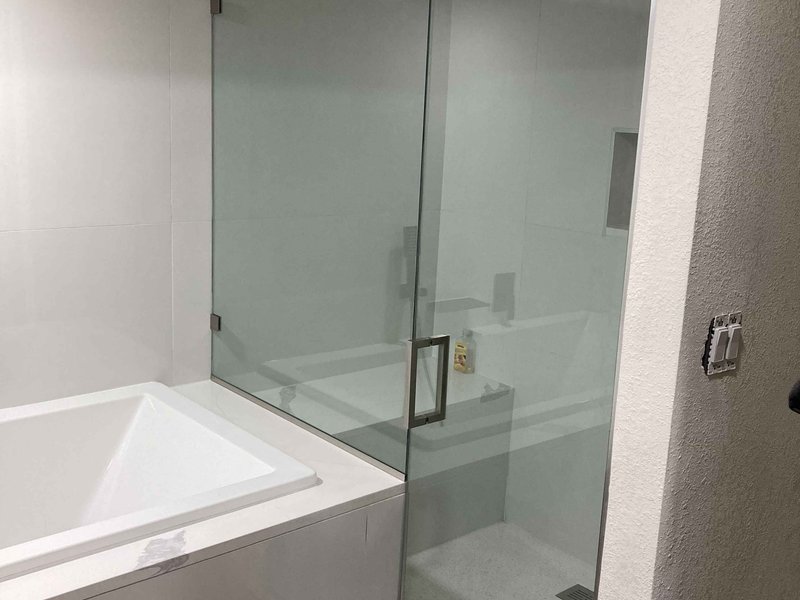 Frameless steam shower with brushed nickel clips beside a soaking tub