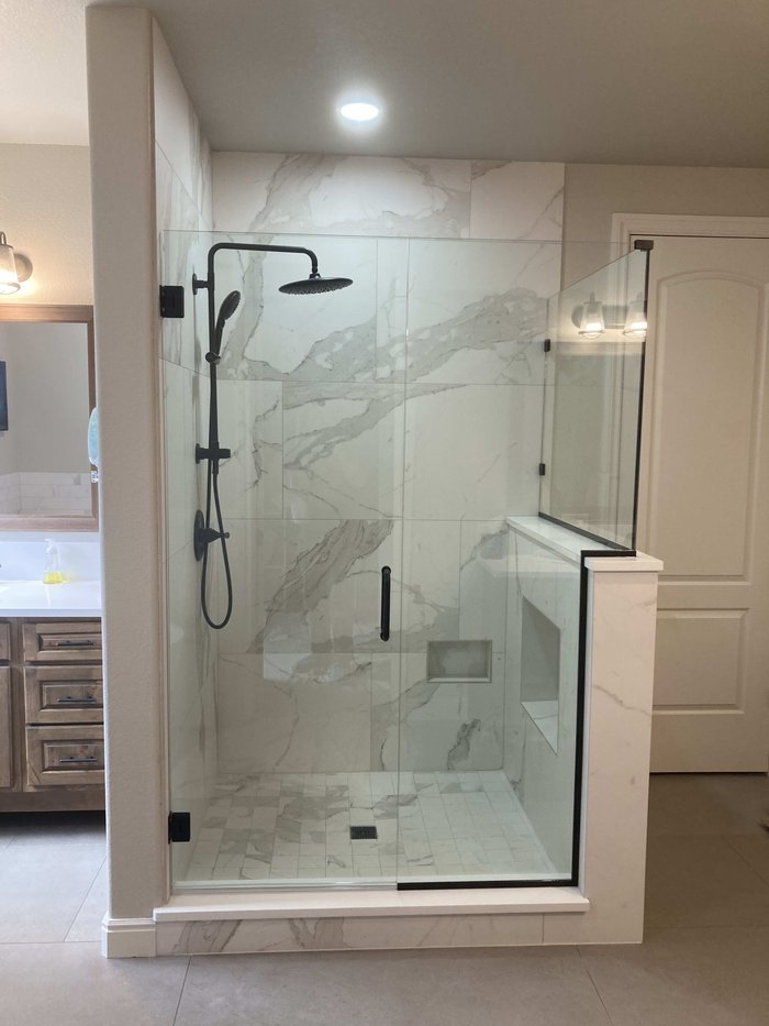 Frameless step-up return shower with matte black hardware and marble tile