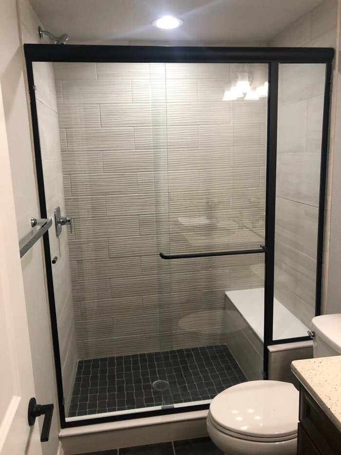 Semi-frameless bypass slider shower with matte black hardware, built-in seat, and textured tile