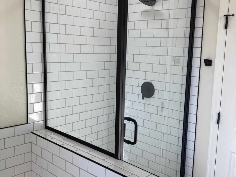 Semi-frameless matte black shower enclosure beside a soaking tub with subway tile