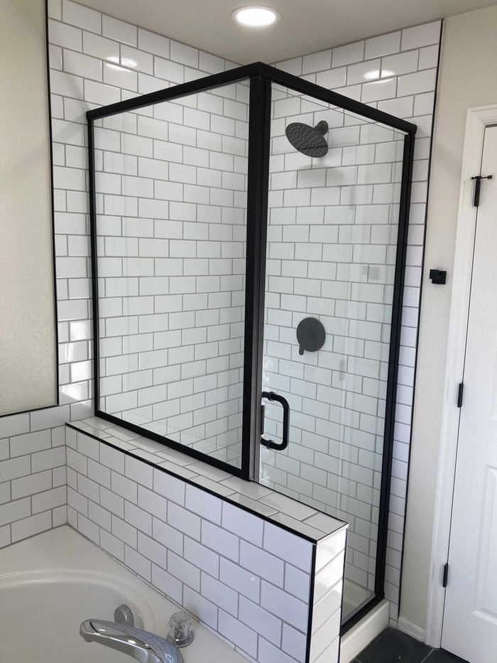 Semi-frameless matte black shower enclosure beside a soaking tub with subway tile