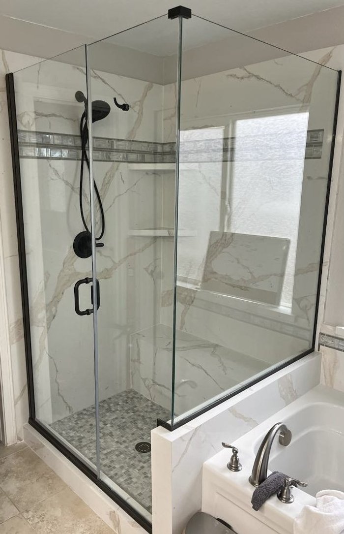 Semi-frameless Silhouette Elite shower with matte black hardware beside a marble soaking tub
