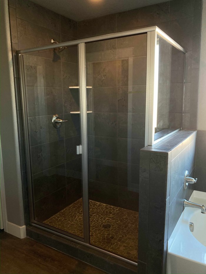 Semi-frameless swing-door shower with buttress panel, chrome hardware, and dark tile